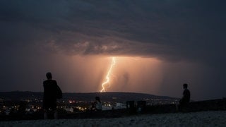 Menschen schauen sich auf einem Aussichtspunkt eine heraufziehende Gewitterfront an.