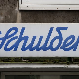 Der Schriftzug "Schulden" hängt über einem leeren Ladenlokal. 