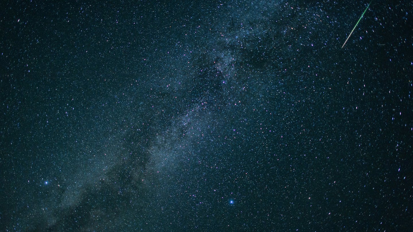 Eine Sternschnuppe leuchtet neben der Milchstraße am Nachthimmel.