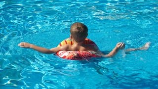 Ein kleiner Junge mit Schwimmring planscht in einem Freibadbecken (Symbolbild).