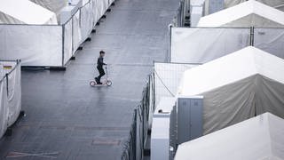 Ein kleiner Junge fährt auf einem Roller durch eine Notunterbringung für Geflüchtete.