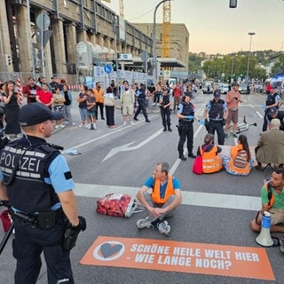 Aktivisten der Gruppe Letzte Generation sitzen bei einer Blockade auf der Straße vor dem Hauptbahnhof.