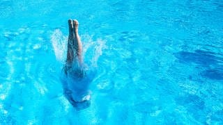 Eine Frau tauch mit einem Kopfsprung in ein Schwimmerbecken ein.