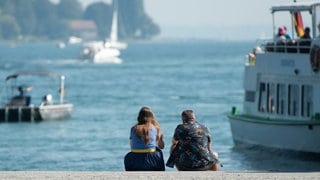 Menschen sitzen bei Sonnenschein am letzten Tag der Sommerferien in Baden-Württemberg an der Promenade.