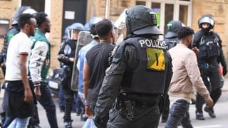 Eine Gruppe von Menschen wird nach Ausschreitungen bei einer Eritrea-Veranstaltung von Polizeikräften eskortiert. 