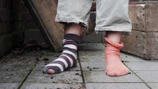 Ein zehn Jahre altes Mädchen steht in abgetragener Kleidung ohne Schuhe in einem Hinterhof.