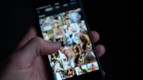 Ein Mensch schaut sich auf einem Smartphone pornografische Bilder an. 