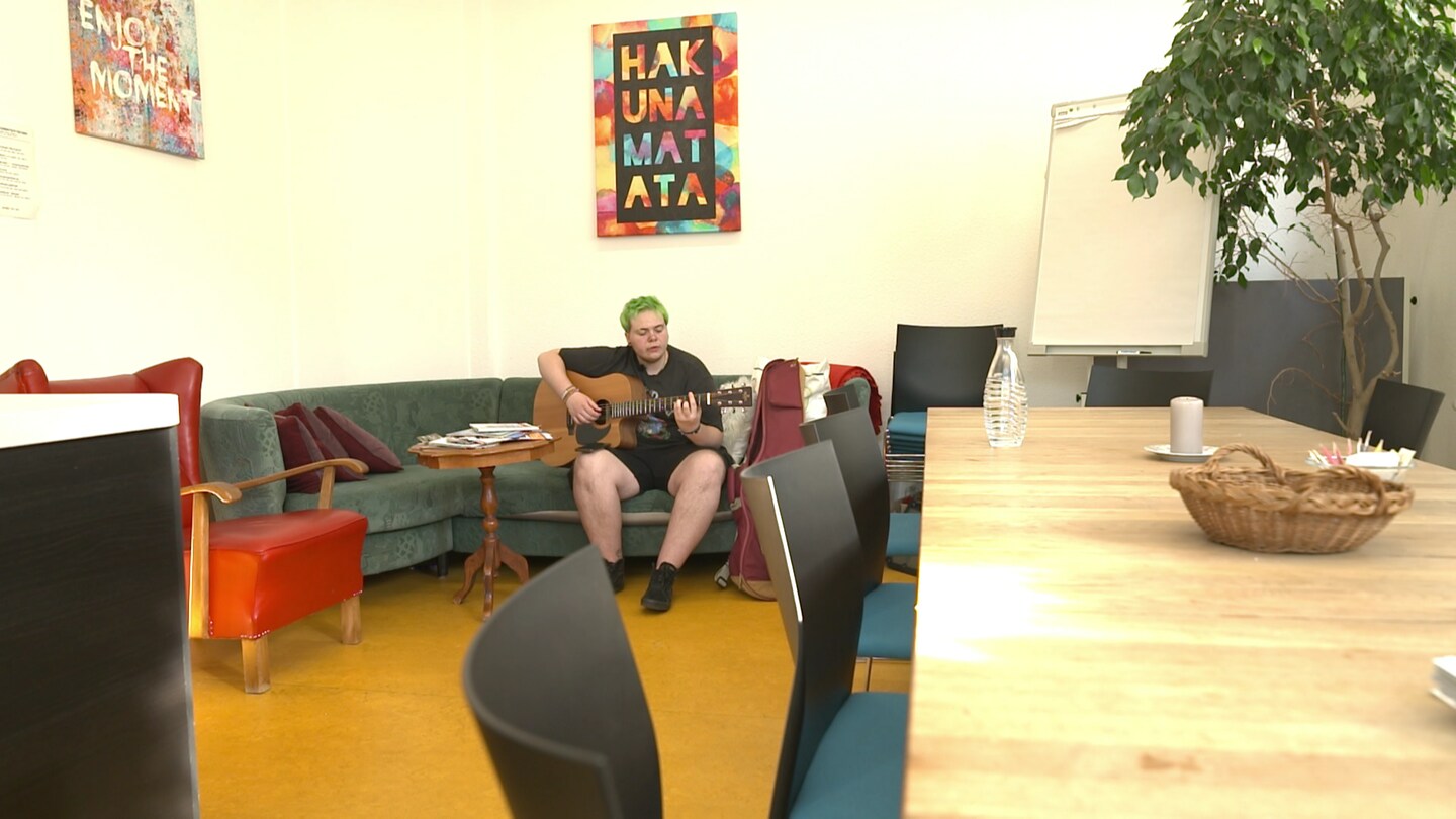 Ein junger Mann sitzt auf einem Sofa und spielt Gitarre.