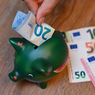 Ein Mädchen steckt einen 20-Euro-Schein in ein Sparschwein (Symbolbild).