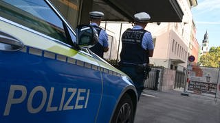 Zwei Polizisten stehen mit ihrem Streifenwagen vor einer Synagoge in Stuttgart. 