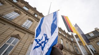 Die Flagge Israels wird von einem Mitarbeiter des Staatsministeriums Baden-Württemberg zwischen den Flaggen der EU, Deutschlands und Baden-Württembergs gehisst. 