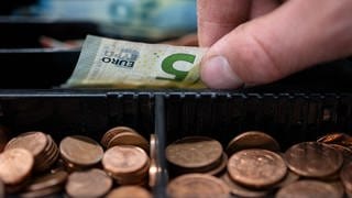 Ein Mitarbeiter eines Einzelhandelsgeschäfts nimmt einen 5-Euro-Schein aus einer Einkaufskasse.