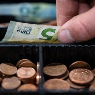 Ein Mitarbeiter eines Einzelhandelsgeschäfts nimmt einen 5-Euro-Schein aus einer Einkaufskasse.