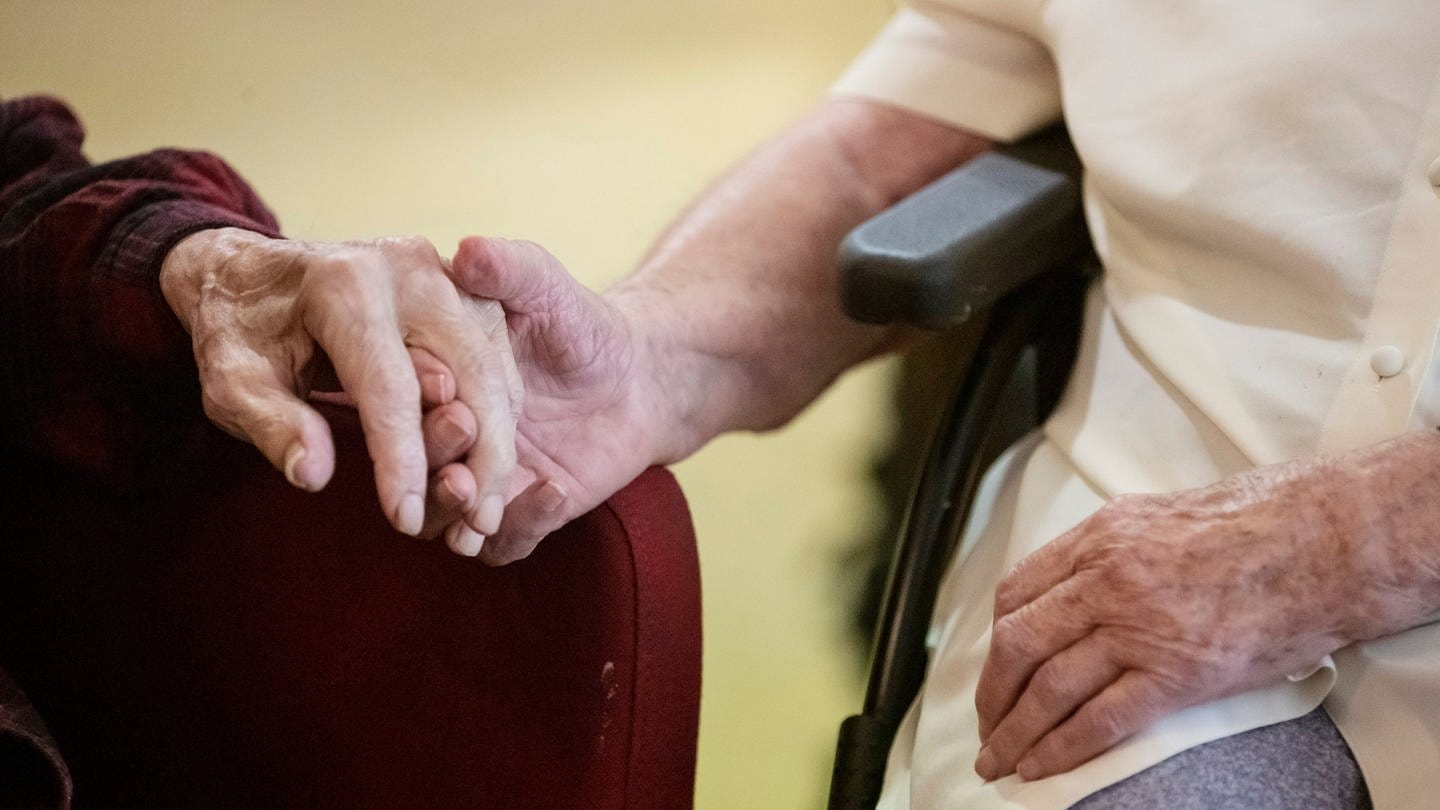 Eine Bewohnerin und ein Bewohner halten in einer Demenz-Wohngemeinschaft die Hände.