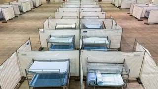 Stockbetten stehen zwischen Zäunen in einer Notunterkunft für Asylsuchende: Städte und Gemeinden in BW suchen händeringend nach Unterkünften für Geflüchtete (Symbolbild).