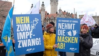 Teilnehmerinnen einer Demonstration von Gegnern und Gegnerinnen der Coronamaßnahmen der Bundesregierung halten Schilder mit dem Logo des Senders "AUF1" hoch. Auf den Schildern stehen die Slogans "Nein zum Impfzwang" und "Nehmt die Masken ab" (Archivbild).