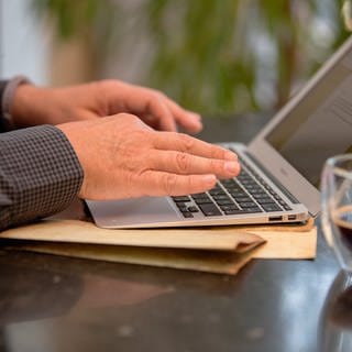 Ein Mann sitzt in seiner Wohnung am Laptop. In vielen Ballungsräumen ist die Nachfrage nach Immobilien und Wohnungen groß, das nutzen auch Betrüger.