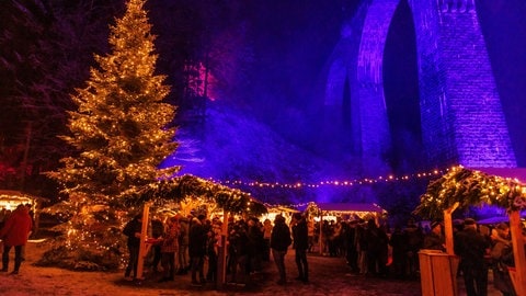 Menschen stehen zwischen Verkaufsständen auf dem Weihnachtsmarkt in der Ravennaschlucht, der unter einem Aquädukt stattfindet. 