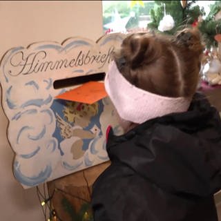 Ein kleines Mädchen wirft einen Brief in den Himmelsbriefkasten