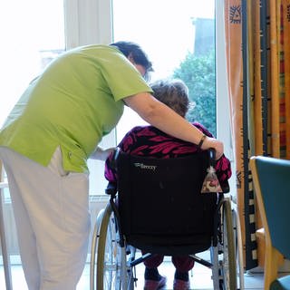 Pflegerin beugt sich über Frau in Rollstuhl