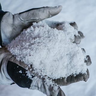 Ein Kraftfahrer im Winterdienst hält Streusalz in den Händen. 