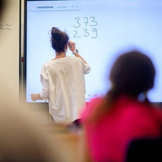 Ein Lehrerin schreibt eine Mathematikaufgabe auf eine digitale Schultafel im Klassenraum einer 4. Klasse einer Grundschule. 