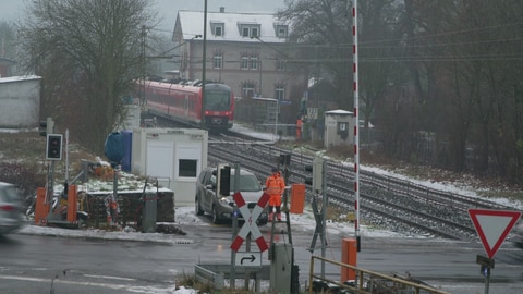 Am Bahnübergang in Grünsfeld (Main-Tauber-Kreis) steht ein Bahnmitarbeiter an der offenen Schranke.