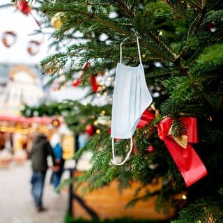 Eine Corona-Maske hängt an einem verzierten Weihnachtsbaum