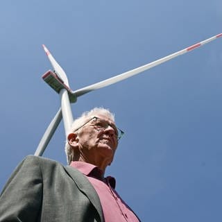 Archivbild: Winfried Kretschmann (Grüne) steht bei einer Besichtigung einer Baustelle einer Windkraftanlage vor einem schon gebauten Windrad. (Mai 2023)