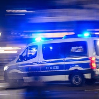 Ein Mannschaftswagen der Polizei fährt mit Blaulicht durch die Nacht.