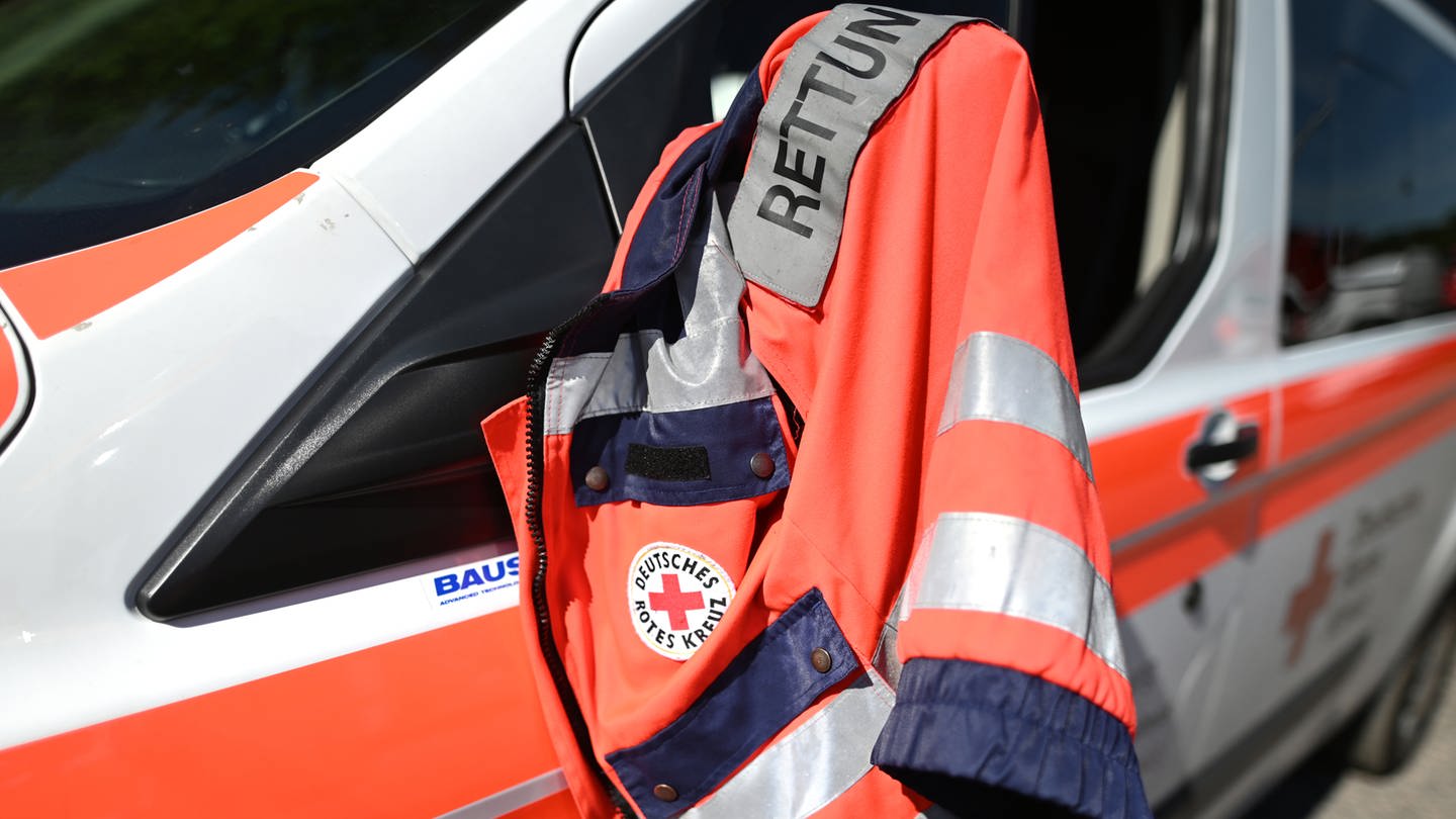 Die Jacke eines Rettungssanitäters des Deutschen Roten Kreuzes hängt am Fenster eines Krankenwagens.