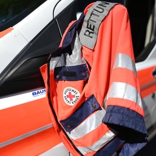 Die Jacke eines Rettungssanitäters des Deutschen Roten Kreuzes hängt am Fenster eines Krankenwagens.