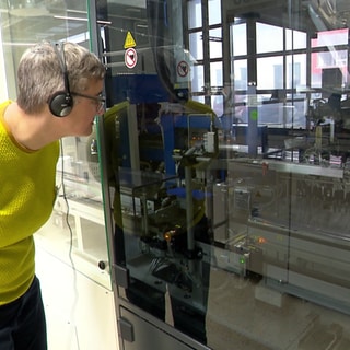 Mann sieht in eine Maschine hinein, die hinter einer Glaswand ist