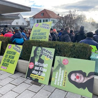Protestplakate gegen die Grünen liegen am Rande der Demonstration im baden-württembergischen Biberach auf dem Boden oder sind an eine Hecke gelehnt.