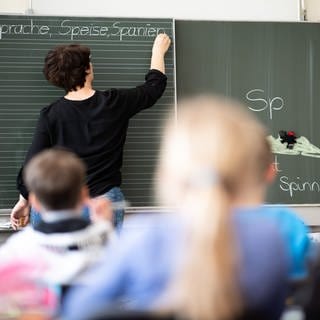 Eine Lehrerin schreibt in einer Grundschule Wörter mit "Sp" am Anfang an eine Tafel. 
