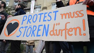 Klimaaktivisten der "Letzten Generation" protestieren vor dem Oberlandesgericht (OLG) Karlsruhe mit einem Plakat auf dem steht "Protest muss stören dürfen!". 