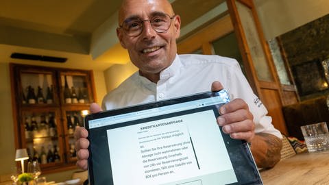 Sommelier Holger Baier zeigt im Sternerestaurant "bi:braud" in Ulm auf einem Tablet die Reservierungsseite des Lokals, auf der über eine Stornogebühr informiert wird.