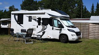 Ein Wohnmobil steht auf einem Campingplatz. Vor dem Mobil stehen ein Tisch und Stühle.