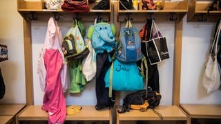 Taschen und Kleidung von Kindern hängen an der Garderobe in einer Kita