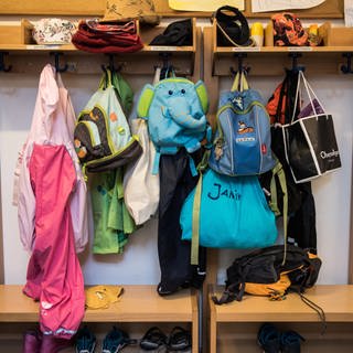 Taschen und Kleidung von Kindern hängen an der Garderobe in einer Kita