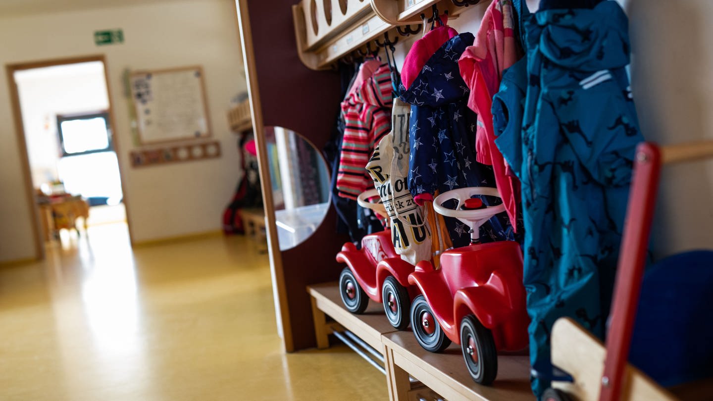 Bobbycars stehen unter Jacken von Kindern, die an einer Garderobe einer Kindertagesstätte (Kita) hängen.
