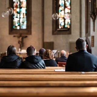 Menschen sitzen bei dem Gottesdienst in den Kirchenbänken der Leonhardskirche in Stuttgart.