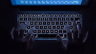 Ein Mann benutzt die beleuchtete Tastatur eines Notebooks (Szene gestellt)