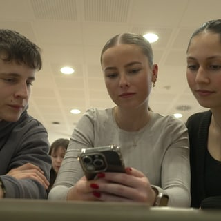 Drei Schüler schauen auf ein Smartphone.