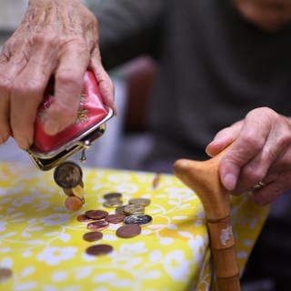Eine Rentnerin schüttet Kleingeld aus einer Geldbörse auf den Küchentisch.