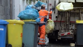 Ein Mitarbeiter der Entsorgungsbetriebe wirft Abfall in ein Müllfahrzeug