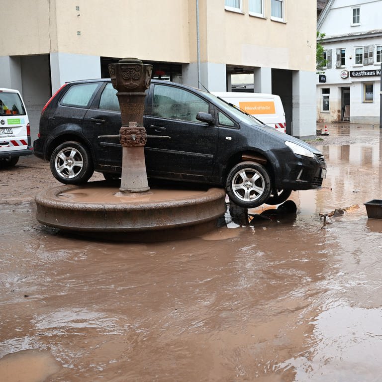 Auf einem Brunnen in Rudersberg steht ein durch ein Hochwasser weggespültes Auto. Seit Tagen kämpfen die Helfer in Bayern und Baden-Württemberg gegen die Flut und ihre Folgen.