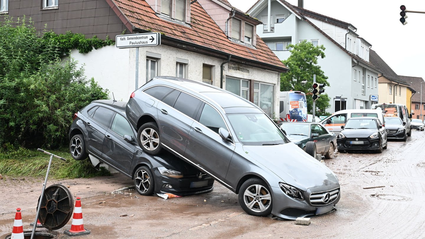 Auf einer Straße in Miedelsbach stehen Fahrzeuge, die durch ein Hochwasser nach einem Unwetter weggespült wurden.