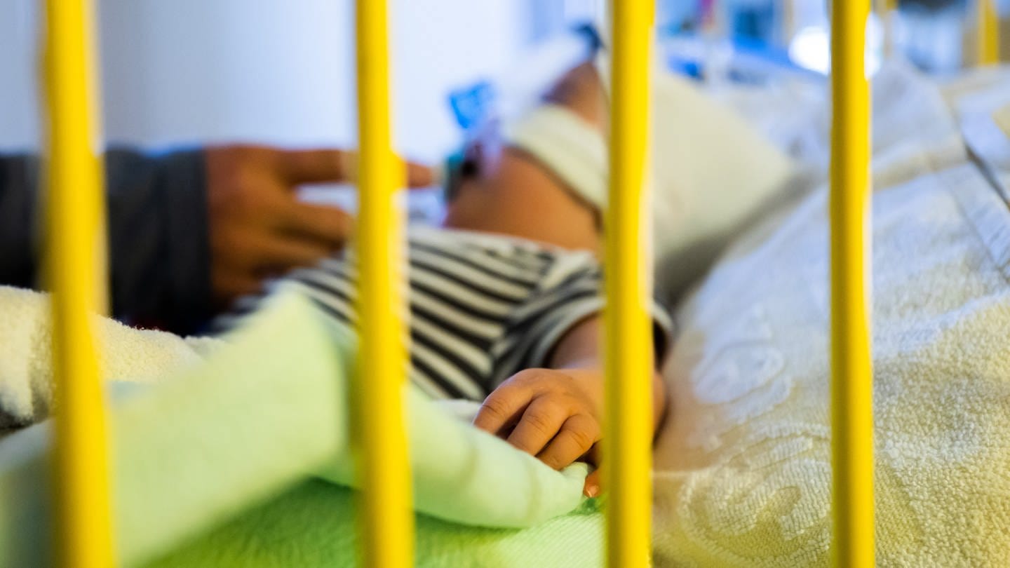 Ein Vater streichelt seinen achteinhalb Monate alten Sohn, der mit einem Atemwegsinfekt auf der Intensivstation einer Kinderklinik liegt und non-invasiv beatmet wird (Archivbild).