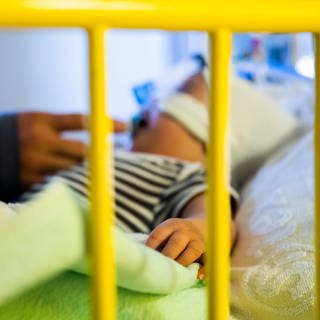 Ein Vater streichelt seinen achteinhalb Monate alten Sohn, der mit einem Atemwegsinfekt auf der Intensivstation einer Kinderklinik liegt und non-invasiv beatmet wird (Archivbild). 